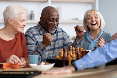 Emotional black man playing chess with multiracial friends clipart