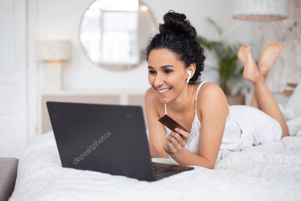 Happy pretty millennial european brunette lady with wireless headphones doing online shopping in laptop