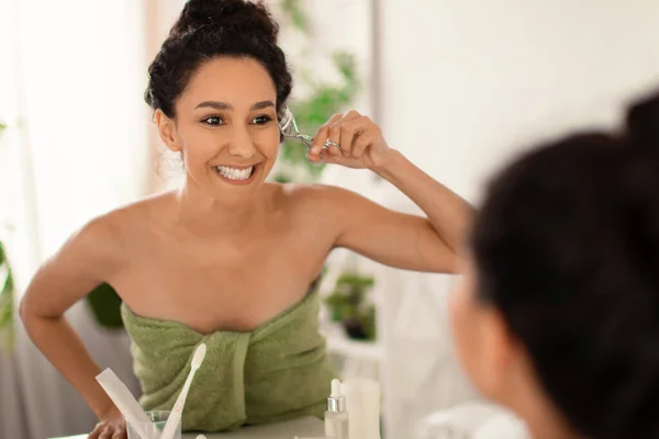 Mulher bonita usando frisador de pestanas na frente do espelho em casa, espaço livre — Fotografia de Stock