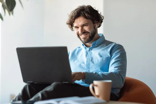 Glimlachende zakenman met laptop zittend op zitzak in het kantoor — Stockfoto