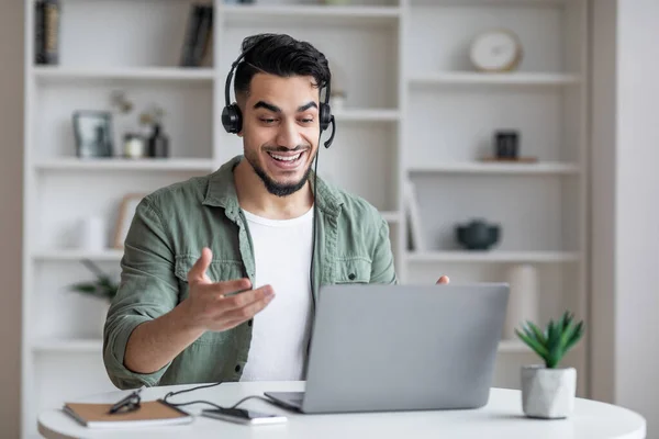 Tutoría en línea. Hombre árabe sonriente en auriculares teniendo videoconferencia en el ordenador portátil —  Fotos de Stock