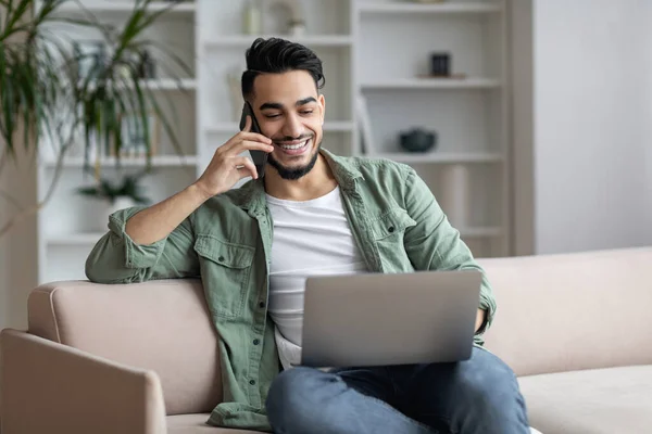 Zdalny biznes. Arab mężczyzna freelancer rozmawiając przez telefon i za pomocą laptopa — Zdjęcie stockowe