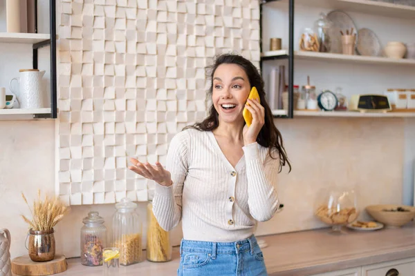 Nadšený žena mluví na smartphone, zatímco stojí ve světle moderní kuchyně interiéru, s emocionální konverzaci — Stock fotografie