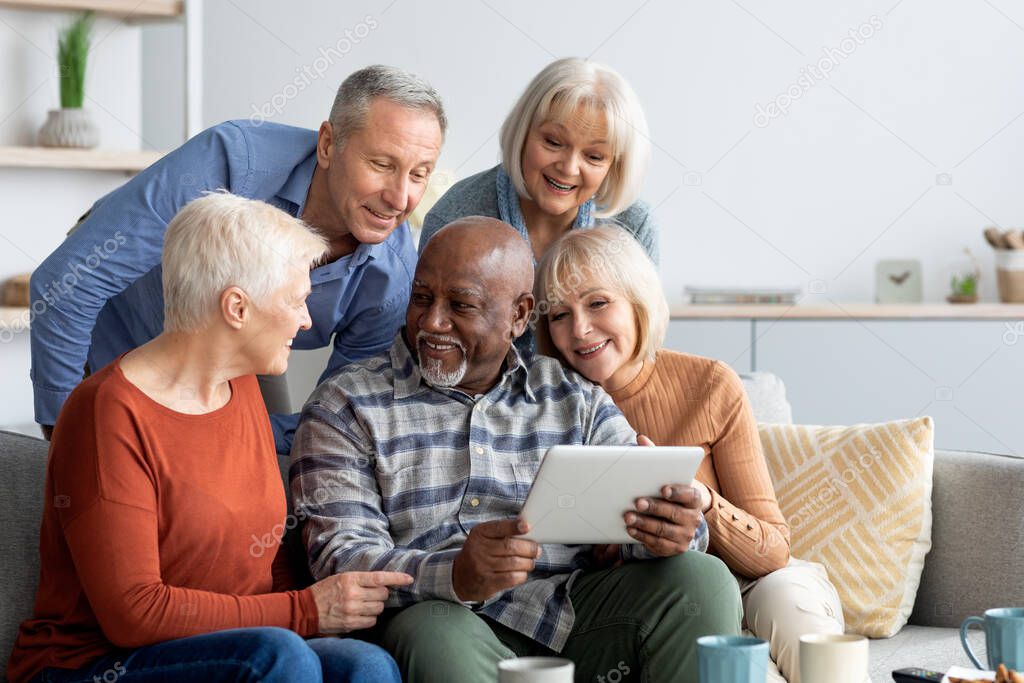 Cheerful elderly people spending time together at home, using gadgets