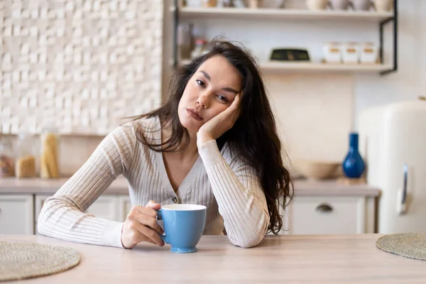 Mujer cansada y soñolienta tomando café por la mañana, sintiéndose agotada, sufriendo de insomnio, sentada en la cocina — Foto de Stock