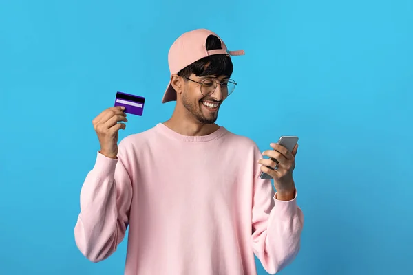 Chico indio alegre sosteniendo el teléfono celular y la tarjeta de crédito —  Fotos de Stock