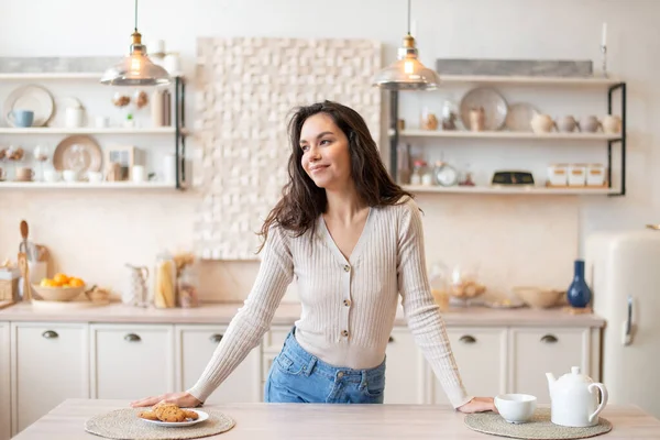 Happy hospodyňky stojí v kuchyni interiéru u stolu, dívá se jinam a usmívá se, pózuje v moderním interiéru domu — Stock fotografie