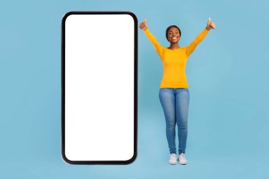 Mutlu, heyecanlı, binlerce yıllık Afro-Amerikan kadın, gündelik şov programında parmaklarını kaldırıp boş ekranlı akıllı telefonuyla ayakta duruyor.