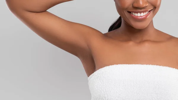 Feliz milenar afro-americana fêmea com pele perfeita em toalha mostrando axila isolada em fundo cinza — Fotografia de Stock