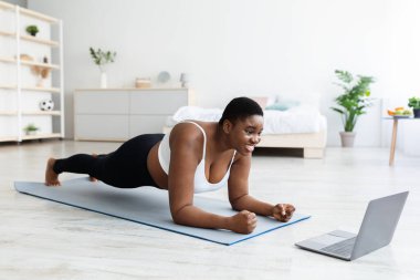 Çevrimiçi spor ve kilo kaybı. Kilolu genç siyahi kadın evde dizüstü bilgisayarın önünde egzersiz yapıyor.