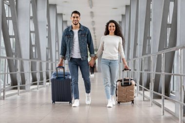 Seyahat zamanı. Havalimanı Terminali 'nde bavulla yürüyen neşeli bir Arap çift.