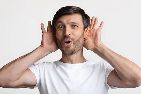 Hombre curioso sosteniendo las manos cerca de los oídos Noticias de escucha, Fondo blanco — Foto de Stock