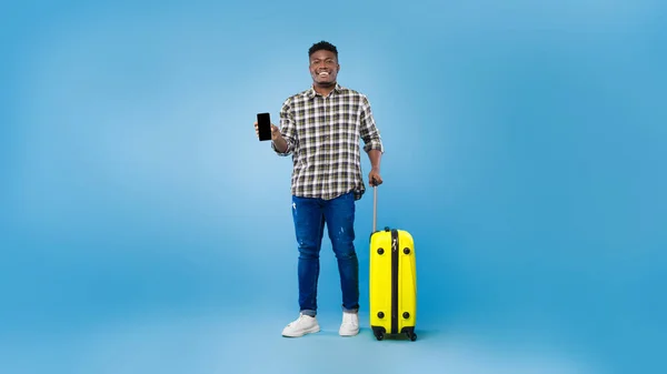 밝은 가방을 가진 행복 한 젊은 흑인 남자가 푸른 스튜디오 배경에 빈 화면으로 스마트폰을 시연 — 스톡 사진