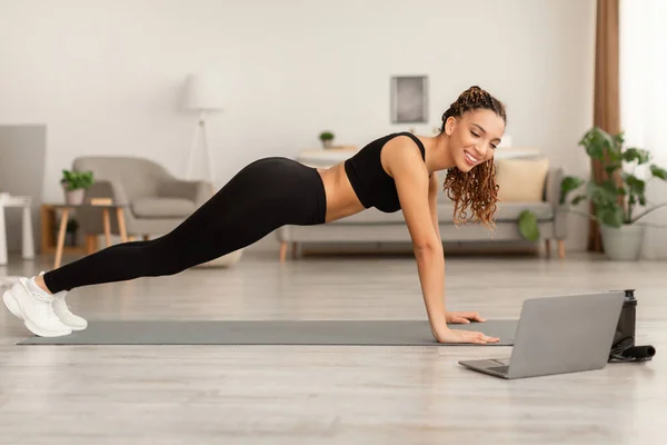 Afrikaanse dame in de buurt van laptop staande in Plank Oefening Thuis — Stockfoto