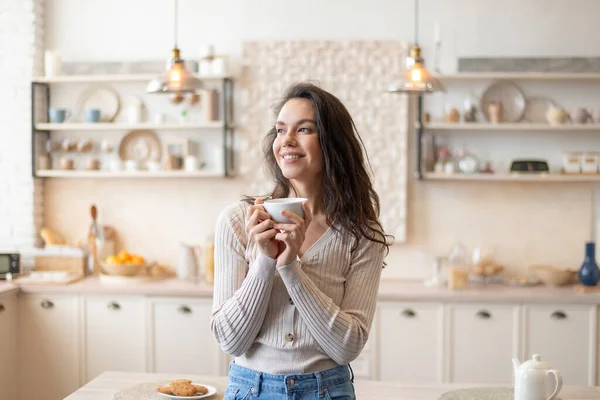 Begin van de dag. Portret van een vrolijke vrouw die 's ochtends koffie drinkt, beker in handen houdt, in de keuken staat — Stockfoto