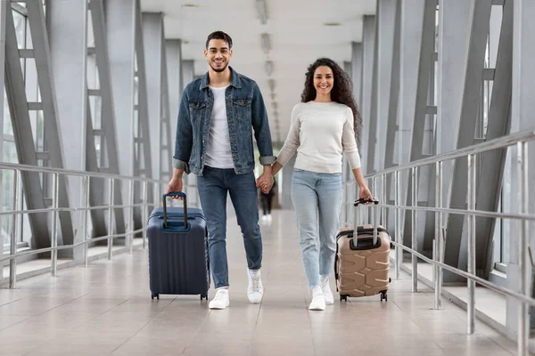 Seyahat zamanı. Havalimanı Terminali 'nde bavulla yürüyen neşeli bir Arap çift.