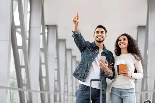 Coppia araba con passaporti e biglietti in piedi all'aeroporto e indicando lontano — Foto Stock