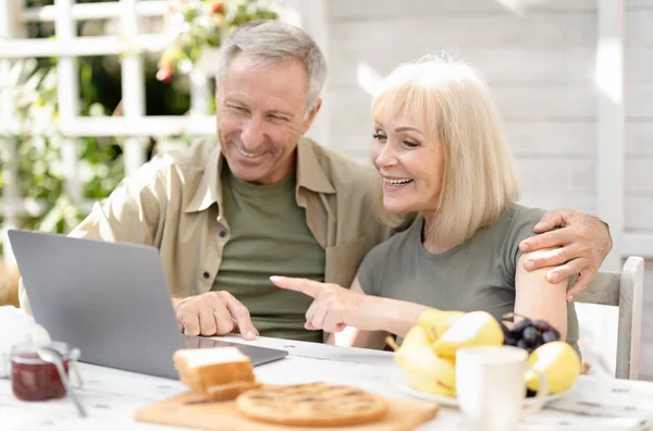 Modern emeklilik yaşam tarzı konsepti. Mutlu yaşlı çift dizüstü bilgisayar kullanıyor, internette geziniyor, dışarıda oturuyor. — Stok fotoğraf