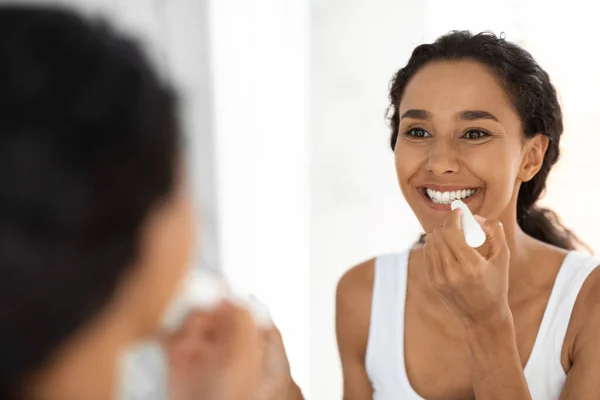 Menina bonita olhando para o espelho e aplicando hidratante Lip Balm — Fotografia de Stock