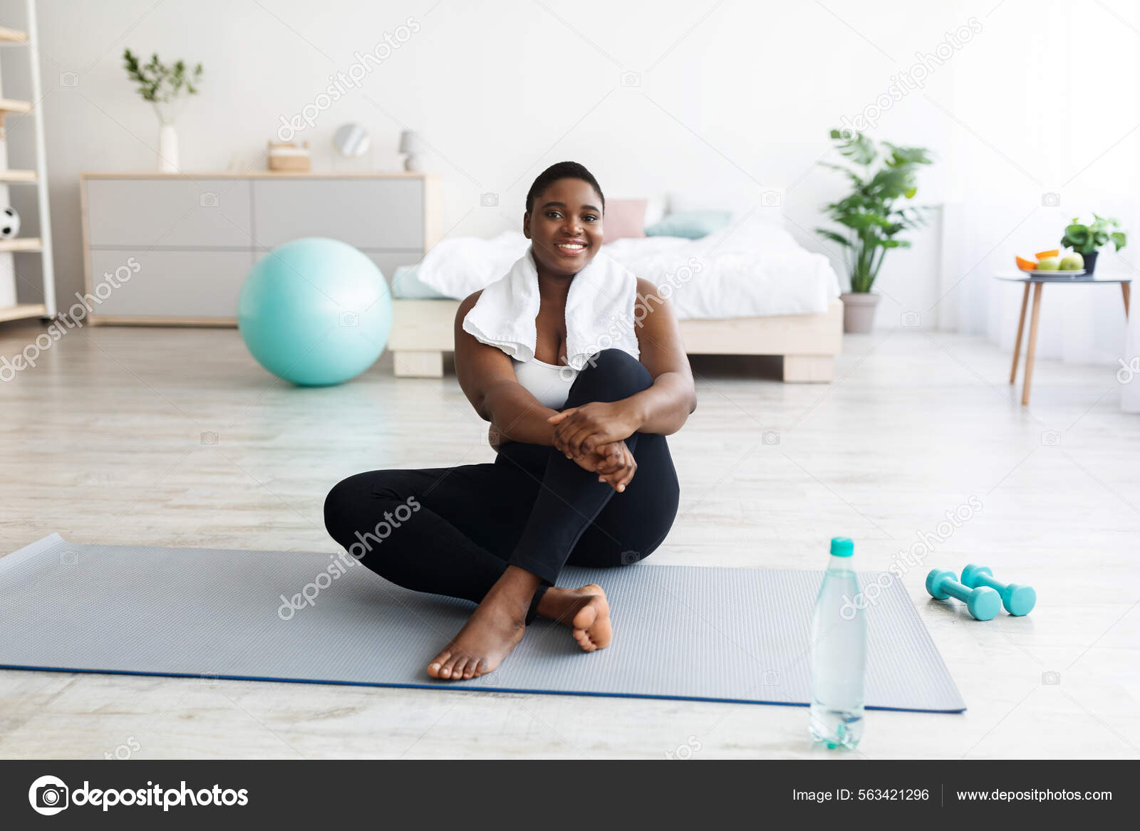 Smiling overweight young black woman sitting on yoga mat, resting