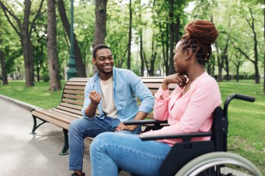 Tekerlekli sandalyedeki neşeli genç siyahi kadın şehir parkında erkek arkadaşıyla konuşuyor.