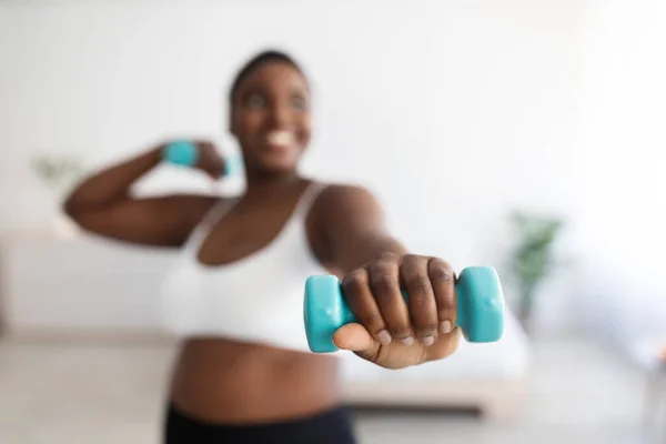 Además de tamaño joven mujer negra haciendo ejercicios con pesas, fortaleciendo su cuerpo en casa, enfoque selectivo — Foto de Stock