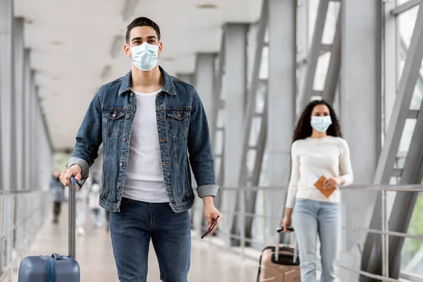 Hombre y mujer usando máscaras faciales mientras camina con equipaje en el aeropuerto —  Fotos de Stock