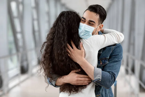 Hombre árabe con máscara médica abrazando a su novia en el aeropuerto después de la llegada —  Fotos de Stock