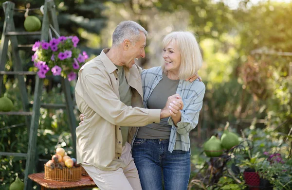 Радісні старші подружжя танцюють в саду, тримаючи руки і сміючись, насолоджуючись проведенням часу разом на відкритому повітрі — стокове фото