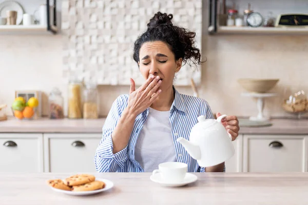 Slaperige vermoeide vrouw die vroeg wakker wordt, thee in beker en gaap giet, zittend in modern keukeninterieur, kopieerruimte — Stockfoto