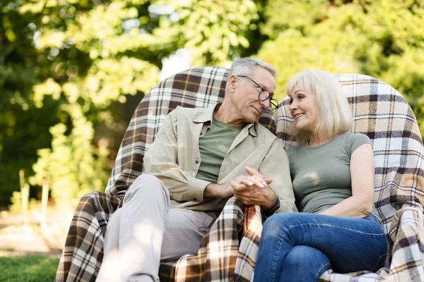 Amar pareja de ancianos casados descansando en su jardín en el campo, sentado en sillas de mimbre y mirándose el uno al otro —  Fotos de Stock