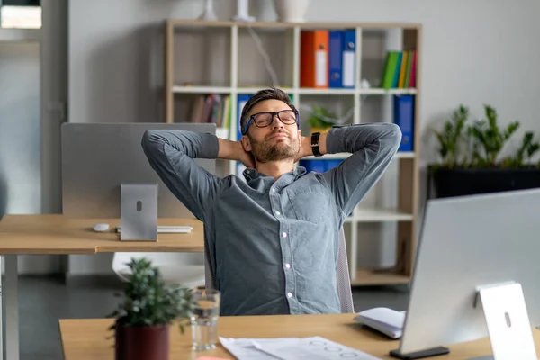 A fazer uma pausa. Homem de meia idade relaxando na cadeira sentado no local de trabalho e descansando no escritório, inclinando-se para trás — Fotografia de Stock