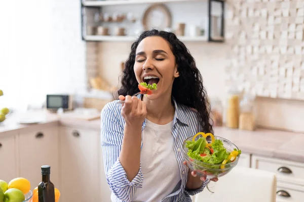 Idea zdrowego odżywiania. Podekscytowana kobieta ciesząca się świeżej sałatki warzywnej, jedząc kolację w kuchni w domu — Zdjęcie stockowe