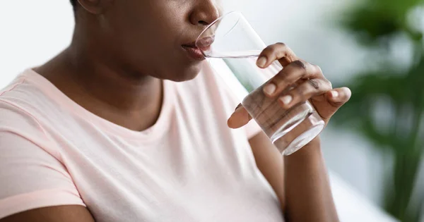 Vista ritagliata di sovrappeso nero femminile bere acqua minerale da vetro all'interno, panorama — Foto Stock