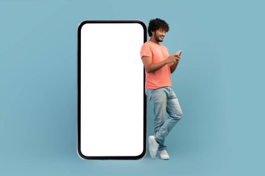 Havalı Hintli adam cep telefonu kullanarak büyük bir akıllı telefona yaslanıyor.