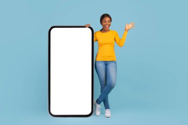 Gülümseyen duygusal, bin yıllık Afro-Amerikan kadını, boş ekranlı, büyük akıllı telefonuyla gündelik yerinde duruyor.