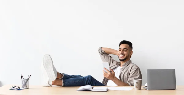 Arabo uomo a riposo piedi sul tavolo utilizzando il telefono cellulare — Foto Stock