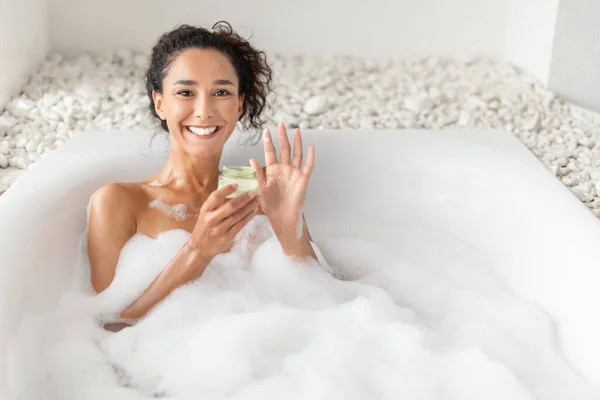 Atrakcyjna młoda kobieta leżąca w gorącej kąpieli z bąbelkami, stosująca krem lub maskę do włosów w domu, wolna przestrzeń — Zdjęcie stockowe