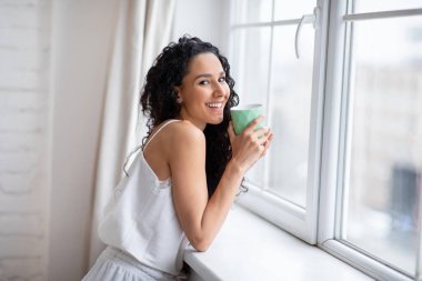 Uzun saçlı, pijamalı esmer bayanın yatak odasının penceresinin yanında sıcak çay içmesine sevindim.