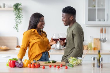 Mutfakta vakit geçirirken ellerinde şarap bardaklarıyla romantik siyah bir çift.