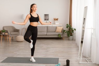 Yoga yapan kadın tek bacaklı poz veriyor, içeride meditasyon yapıyor.