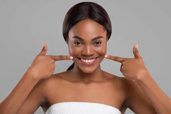 Cheerful pretty black woman wrapped in towel pointing fingers at perfect snow white smile — Stock Photo, Image