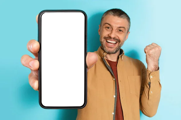 Uomo mostrando grande schermo smartphone gesticolando sì su sfondo blu — Foto Stock