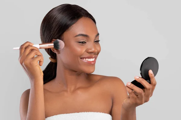 Le ganska ung afrikansk amerikansk kvinna med perfekt hud i handduk tillämpa pulver i ansiktet med makeup borste — Stockfoto