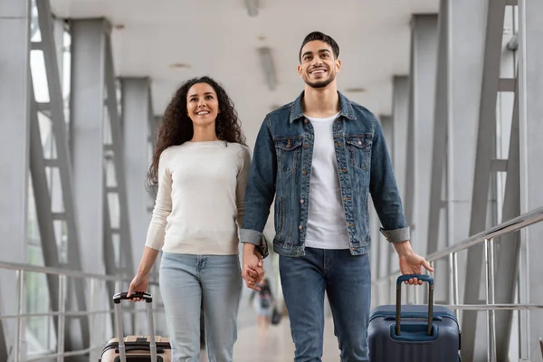 Retrato de pareja árabe milenaria positiva caminando en el aeropuerto con equipaje — Foto de Stock