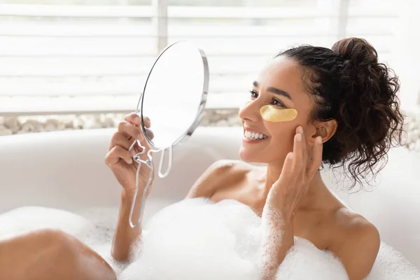 Evde köpüklü banyo yaparken aynanın önüne göz bandı yapıştıran şehvetli genç bayan. — Stok fotoğraf