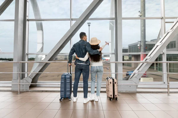 Paar mit Koffer blickt beim Warten auf Flug aus Fenster am Flughafen — Stockfoto