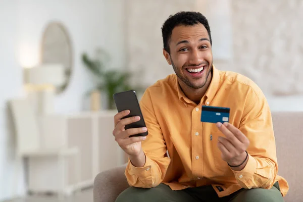 Улыбающийся парень с помощью телефона и кредитной карты дома — стоковое фото