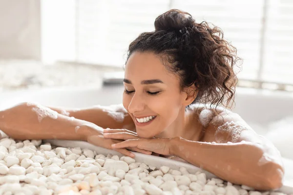 Uśmiechnięta młoda kobieta odpoczywająca w wannie z zamkniętymi oczami, ciesząca się gorącą kąpielą z pianką w domu — Zdjęcie stockowe