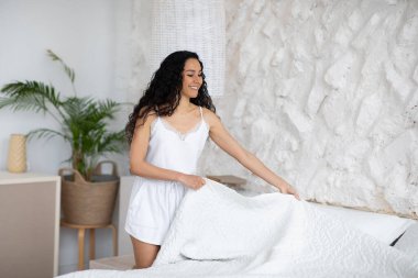 Pijamalı, uzun saçlı, mutlu, beyaz, esmer kadın yatak odasının içini temizliyor.